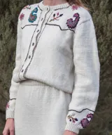 Cardigan tejido de punto color marfil, con bordados artesanales florales y paisley, cierre frontal de botones y detalles de costuras a contratono.