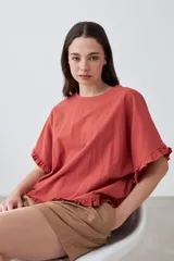 Blusa de corte holgado color salmón, con cuello redondo, mangas cortas con volados y ruedo con detalle de volado.