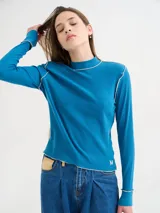 Polera básica de algodón en tejido rib, color turquesa, de manga larga, con hombreras y detalles de pespuntes en color contrastante en las terminaciones y el cuello.