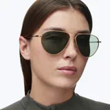 Lentes de sol estilo aviador con montura metálica fina en color dorado y lentes polarizadas en tono verde oscuro. Presentan un diseño clásico con doble puente y terminales de patillas en acetato.