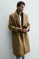Abrigo largo color camel, de corte relajado (relaxed fit), confeccionado en tejido con mezcla de lana. Presenta cuello con solapas de muesca, manga larga, bolsillos de vivo en cadera, bolsillo interior y cierre frontal de botonadura cruzada.