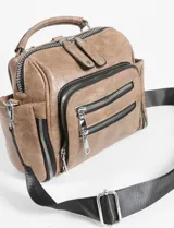 Mochila bandolera de cuero sintético color marrón, con múltiples compartimentos frontales y laterales con cierre metálico. Cuenta con asa superior y correas ajustables para usar como mochila o bandolera.