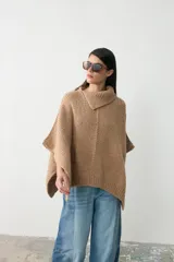 Capita de tejido de punto grueso en color camel, con cuello alto tipo polera y diseño holgado con aberturas laterales para los brazos.