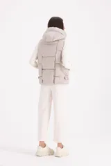 Chaleco acolchado color beige con diseño de cuadros, capucha amplia y cierre frontal oculto.