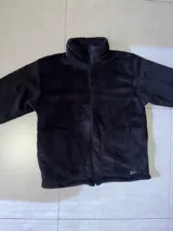 Buzo negro de poliéster con textura de sherpa y cierre frontal.