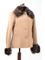 Chaqueta corta color beige confeccionada en lana, con cuello y puños de piel sintética en tonos marrones y negros. Presenta cierre frontal con botones y bolsillos laterales.