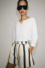 Shorts de tiro medio con trabillas en la cintura y cierre frontal con cremallera y botón. Presenta pliegues delanteros y bolsillos laterales ocultos en la costura, con un diseño de rayas verticales multicolor.
