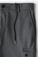 Pantalón cargo gris oscuro de piqué, corte slim fit, con bolsillos laterales con solapa y botón a presión, bolsillos al bies y bolsillos insertados atrás. Cintura clásica con cordón ajustable oculto y elástico revestido atrás.