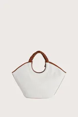 Bolso tipo tote de textura tejida en color blanco, con detalles de ribetes y asas trenzadas en color marrón. Incluye una etiqueta decorativa colgante en el mismo tono de las asas.