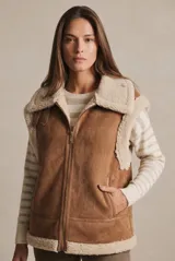 Chaleco estilo gamulán color camel, con interior y bordes de corderito sintético color crema. Presenta cierre frontal metálico, bolsillos laterales y detalles de costuras reforzadas.