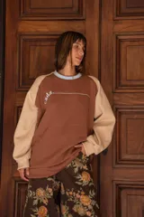 Buzo de corte holgado con diseño bicolor, cuerpo en color marrón y mangas en color beige. Presenta cuello redondo en tono celeste, detalle de costura horizontal en el pecho y puños elásticos.