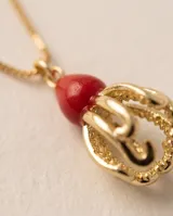 Collar de cadena fina dorada con dije de bronce que combina una piedra roja superior y una estructura esferoide inferior texturizada y calada.