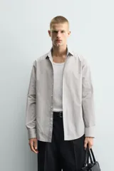 Camisa de corte slim fit confeccionada en tejido de algodón, con estampado de cuadros pequeños en tonos beige y blanco. Presenta cuello italiano, manga larga con puños abotonados y cierre frontal con botones.