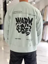 Buzo oversize color verde menta con gran estampado gráfico en la espalda en color negro que dice 'WARM VIBES' y frases complementarias.