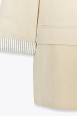 Blazer blanco de lino con cuello solapa, manga larga con hombreras y puños con vuelta estampada. Tiene bolsillos delanteros con solapa y cierre frontal con botón.