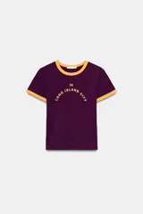 Camiseta de cuello redondo y manga corta, color bordó con detalles en amarillo en cuello y mangas. Presenta un estampado frontal con el texto '74 Long Island City'.