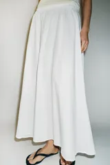 Falda midi de corte en A, color blanco, confeccionada en algodón con cintura elástica de tiro alto y forro interior a tono.