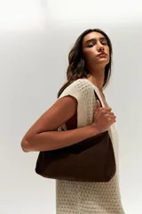 Cartera de hombro tipo baguette confeccionada en gamuza color marrón oscuro, con diseño minimalista y correa integrada.