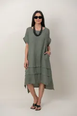 Vestido midi de lino color verde militar, con escote redondo, mangas cortas caídas, bolsillos laterales y falda con detalles de volados horizontales y dobladillo asimétrico.
