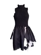Vestido corto negro con corpiño fruncido y cuello alto con volantes. La falda tiene una caída irregular con aplicaciones de cuero y pelo en tonos blancos y negros.