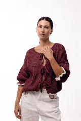 Saco de tejido de punto color bordó con frente abierto y cierre mediante tres lazos frontales. Presenta mangas tres cuartos con terminaciones en volados de color blanco y un diseño de calce holgado.