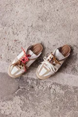 Zuecos de cuero color beige, con cordones marrones y verdes, y detalles de costuras.