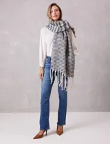 Bufandón de tejido soft con diseño de rayas horizontales en tonos gris y blanco, con terminación de flecos largos en los extremos.