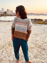 Sweater de lana merino color tostado, con cuello redondo y mangas largas. Presenta un diseño geométrico con motivos étnicos en tonos beige, azul y naranja.