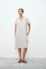 Vestido midi de lino color crudo, con cuello en V, mangas cortas y bolsillos laterales. Diseño holgado y minimalista.