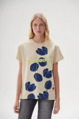 Remera color crema con estampado de flores azules y texto "Blossom" en verde.
