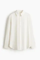 Camisa de manga larga color blanco hueso, con cuello camisero clásico y cierre frontal de botones. Presenta un corte recto y un bajo redondeado.