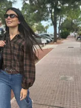 Camisa de corte oversize con estampado de cuadros escoceses en tonos negro y marrón. Presenta cuello camisero, cierre frontal con botones y mangas largas con volumen y puños elásticos.