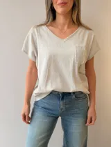 Remera de lino y algodón color beige con escote en V, mangas cortas y calce relajado. Presenta un bolsillo frontal decorado con apliques de strass, encaje y tachas, además de sutiles estampas con escritura manuscrita y detalles desflecados.