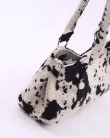 Cartera tipo baguette confeccionada en cuero vacuno con pelo y estampado animal print de vaca. Presenta doble asa de hombro, cierre superior y broches laterales para ajustar su volumen.