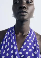 Vestido corto de estilo cruzado con estampado de lunares, cuello en pico y diseño sin mangas. Presenta un lazo lateral para ajuste y falda con caída fluida.