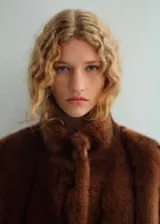 Chaqueta de efecto pelo en color marrón, de corte recto, con cuello alto, mangas largas con puños elásticos y cierre delantero con botones. Cuenta con dos bolsillos de solapa en la parte frontal.