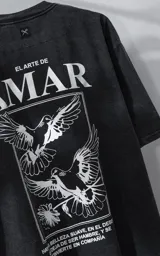 Remera de manga corta con cuello redondo y calce oversize, confeccionada en algodón premium con efecto de lavado nevado. Presenta una estampa gráfica en la espalda con diseño de palomas y texto alusivo.