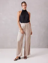 Pantalón palazzo de tiro alto confeccionado en tela satinada. Presenta una pretina delantera con pasadores, cierre y broche, mientras que la parte trasera cuenta con elástico para mayor comodidad. Incluye bolsillos verticales en el frente.