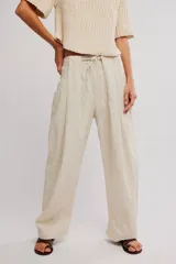 Pantalon de lino y algodon color beige, de tiro bajo, estilo relajado con cintura elastizada ajustable mediante cordón y bolsillos laterales.