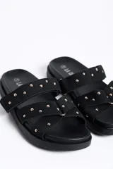 Sandalias negras de doble tira con tachas doradas, suela plana y diseño cómodo.