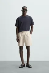 Bermuda de algodón color beige claro, de corte regular fit, con cintura elástica ajustable mediante cordón. Presenta bolsillos laterales y un bolsillo trasero de vivo.