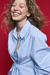 Camisa blanca de manga larga con volumen y estructura, cierre frontal con botones y lazo ajustable en la cintura que realza la silueta.