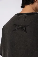 Remeron de corte oversized con cuello redondo y mangas cortas. Presenta un acabado de tela con efecto desgastado y costuras visibles en los bordes, con una etiqueta pequeña en el lateral inferior.