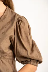 Blusa blanca de algodón con delicado bordado floral, mangas abullonadas de largo 3/4 y cierre frontal con botones y cordón ajustable en la cintura.