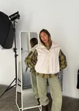 Chaleco color blanco hueso de peluche con cuello alto, cierre frontal con botones a presión y detalles en cuero sintético color beige.