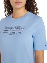 Vestido Tommy Hilfiger celeste de corte recto, con cuello redondo y mangas cortas. Presenta un logo script de la marca estampado en el pecho y la bandera de Tommy Hilfiger bordada en la manga.