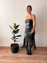 Vestido midi negro de cuerina, corte tubo, strapless, con flecos y abertura en el frente.