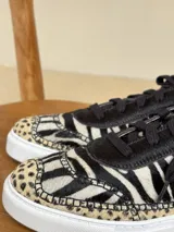 Championes de cuero con diseño de animal print combinado, presentando patrón de cebra en el cuerpo y detalles de leopardo en la puntera. Poseen cordones negros, suela blanca y forro interior en tono nude.