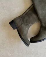 Bota de caña alta confeccionada en cuero vacuno gamuzado color verde oliva, con cierre lateral y taco bajo cuadrado.