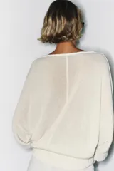 Jersey de punto de color blanco crudo, con escote en V y mangas largas con sisas amplias y puños elásticos acanalados.